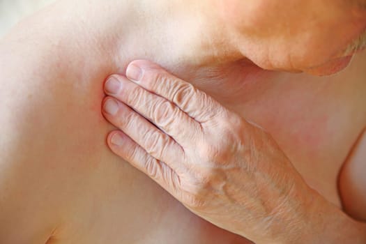 An older man with his hand on an area near his shoulder