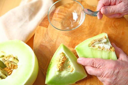A man is ready to seed pieces of ripe honeydew melon over a wood cutting board