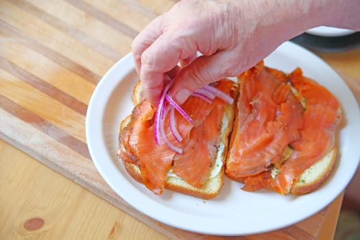 A man puts sliced onions on a salmon sandwich with room for text