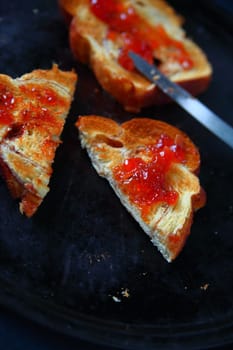 Slices of toast with raspberry jam, one cut in half, on a dark metal baking pan