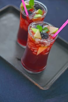 Two chilled sangria cocktails with fresh blackberries and apple pieces on a dark metal tray with copy space