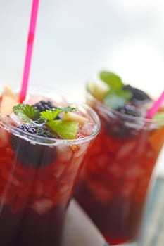 Closeup of two wine cocktails with crushed ice, apple chunks, fresh blackberries and mint with copy space