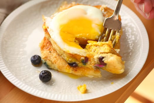 Blueberry pancakes with a fried egg eaten by a man