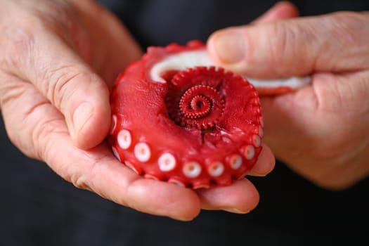 A man holds a reddish-brown octopus tentacle in his hands against a dark background.