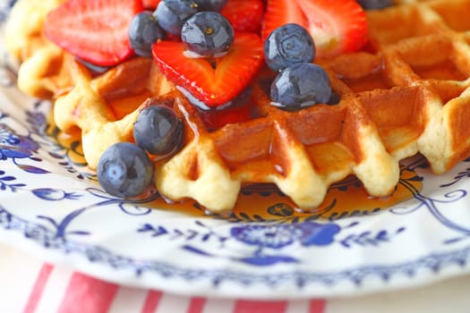 Breakfast waffle with fresh blueberries, strawberries and maple syrup on a decorative plate