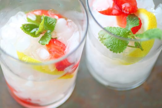 Overhead of two glasses of fruit-infused water with crushed ice, strawberries, lemon and mint