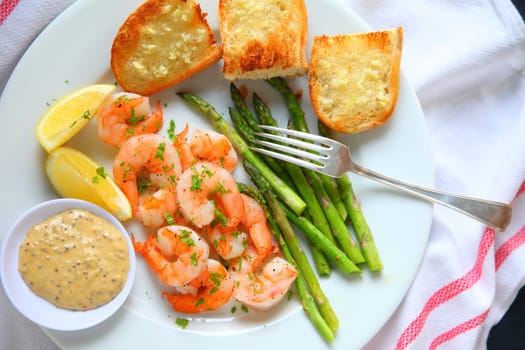 Overhead view of shrimp with asparagus and garlic bread with lemon and a tangy dipping sauce
