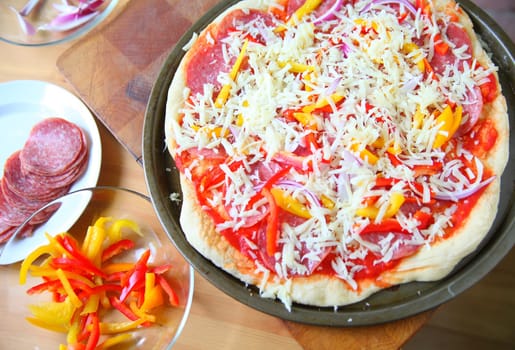 Pizza ready for the oven with dishes of ingredients alongside