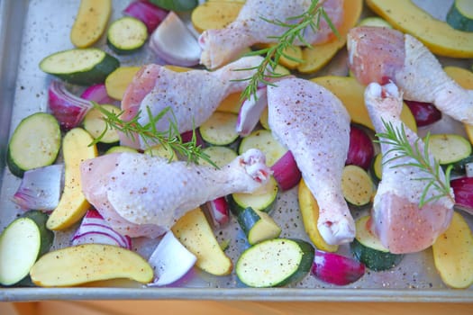 Baking pan with raw chicken legs, zucchini, red onion and fingerling potatoes, seasoned and ready to bake