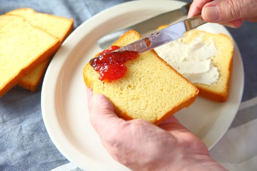 An older man makes a cream cheese and strawberry jam sandwich point of view