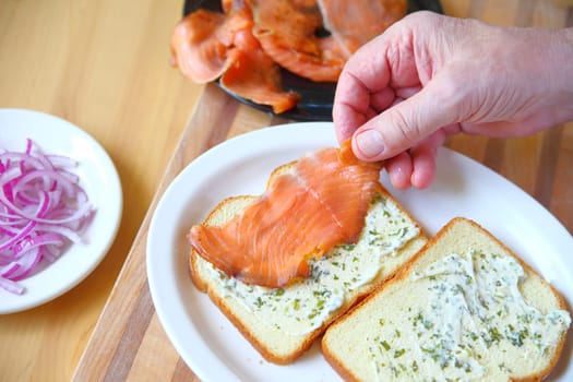 A man puts together a sandwich of smoked salmon and onion on bread with herb mayonnaise