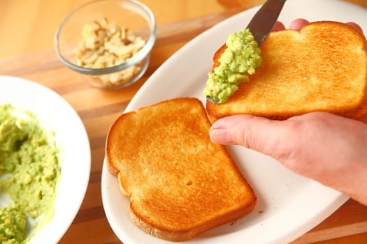 A man spreads mashed avocado on a slice of toast with almond pieces in the background