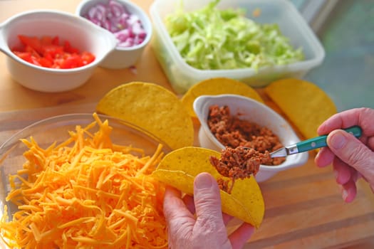 A man makes tacos at home with taco shells, ground beef, lettuce, onions, tomatoes and grated cheese