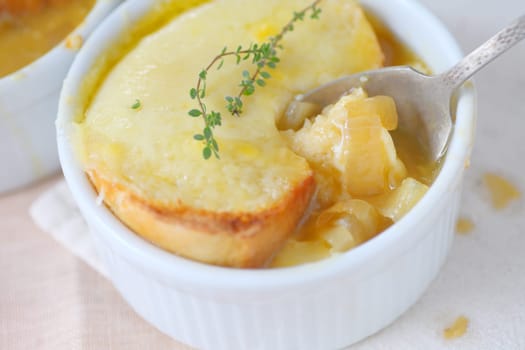 Small bowl of onion soup with melted cheese toast and fresh thyme sprigs on top
