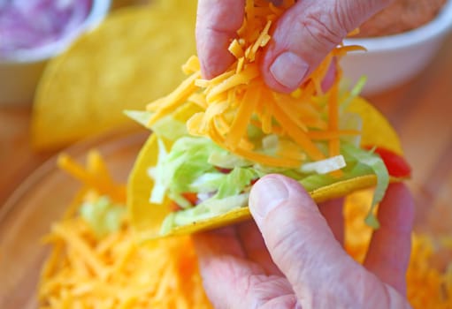 A man adds grated cheese to his homemade taco