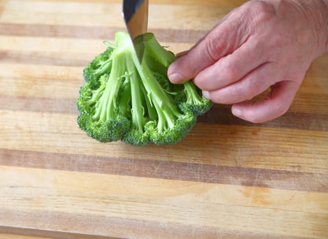 A man cuts up fresh broccoli on a cutting board with room for text