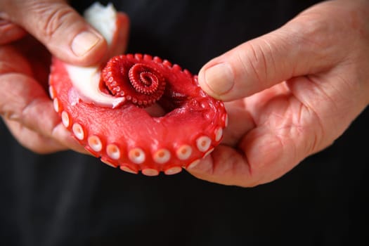 A man in a black apron holds a sashimi octopus tentacle