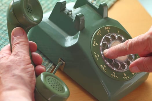 An older man dials a number on a vintage landline phone.
