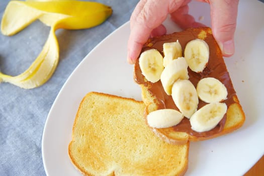 A man holds a slice of toast with creamy chocolate spread and sliced bananas