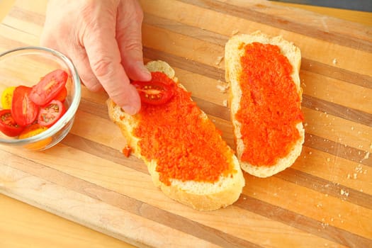 A man places cherry tomatoes on bread spread with tapanade with copy space