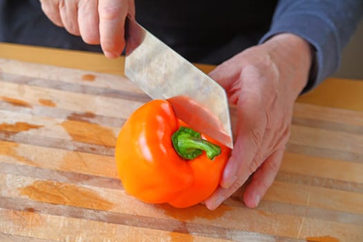 A man begins to cut into an orange bell pepper on a cutting board with copy space