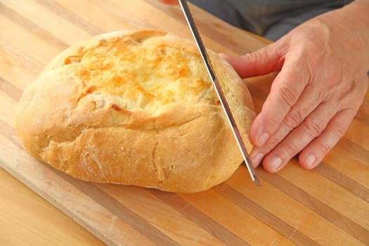 A man begins to cut slices from a loaf of artisan cheese bread