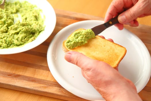 A man spreads mashed avocado on a slice of brioche toast.