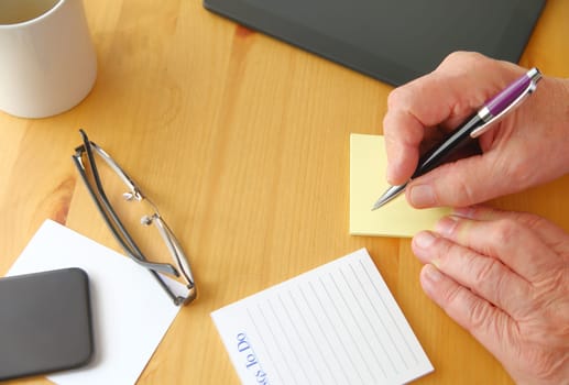 A man holds a pen over a desk with tablet, phone, notepads, glasses, coffee cup and copy space