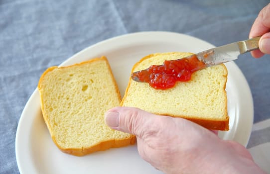 A man puts strawberry jam on a slice of bread with copy space
