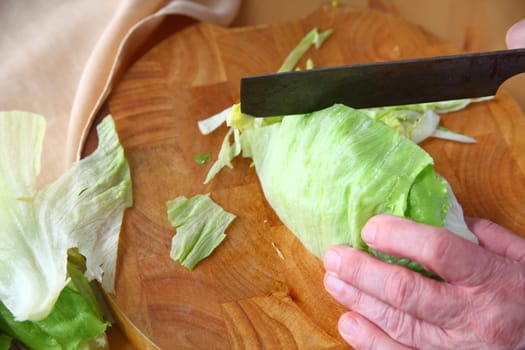 Overhead of man shredding iceberg lettuce on wood cutting board