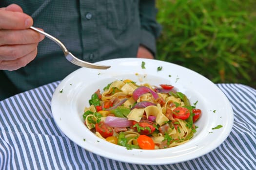 A man eating a meal of noodles with onions, cherry tomatoes and fresh peas on a striped gray and white cloth