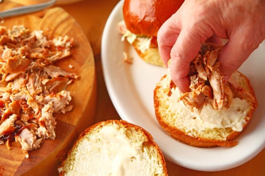 A man puts homemade pulled chicken on a brioche bun