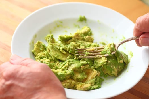 Older man mashes an avocado using a fork point of view