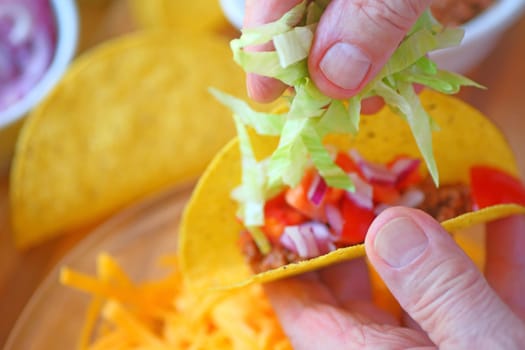 A man adds shredded lettuce to a homemade taco closeup
