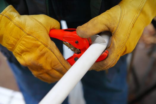Handyman with work gloves makes a cut in a piece of plastic piping.