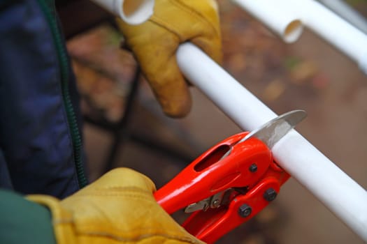 Worker with gloves uses tool to cut a length of PVC pipe