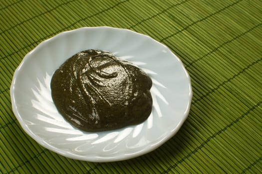 Sauce of basil is on white plate on green background.