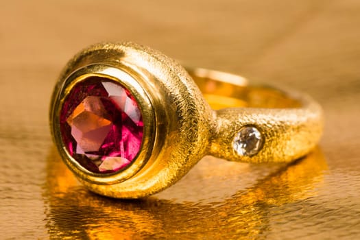 Gold ring with pink gem on golden background.