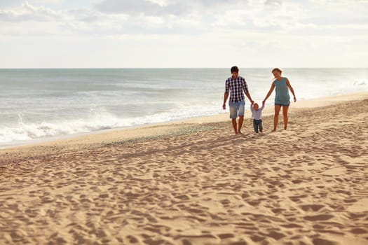 Mother and father with their toddler son walking together on a quiet beach