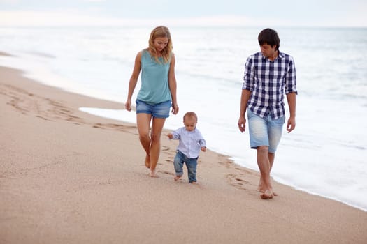 Young couple taking a seaside walk with their toddler