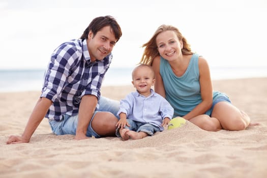 Portrait of two parents and their toddler playing together in the sand at the beach