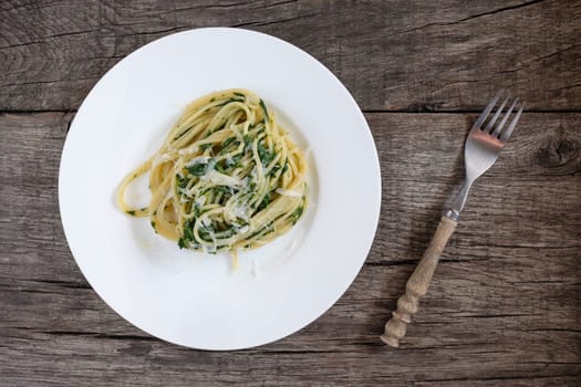 Spaghetti with spinach and Parmesan on a plate and rustic table