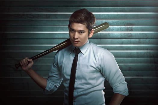 Young asian man with wooden baseball bat standing against dirty background