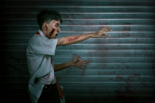 Creepy and bloody asian zombie man with claw hand walking against dirty background