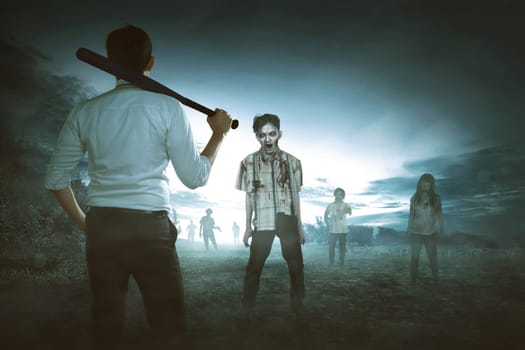 Back view of asian man holding baseball bat against zombies on the scary countryside