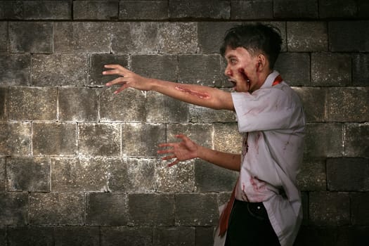 Spooky asian zombie man with wounded face walking against wall background