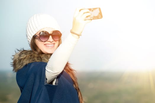 Beautiful happy young girl posing outdoors with phone taking a selfie