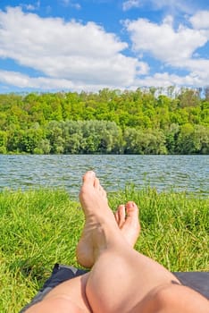 male feet at lake - man relaxing at lake on camping mat - green forest / trees in background