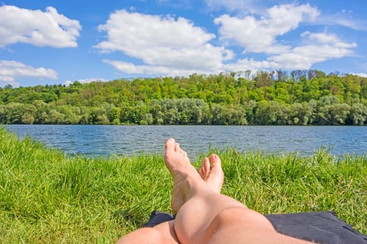 male feet at lake - man relaxing at lake on camping mat - green forest / trees in background