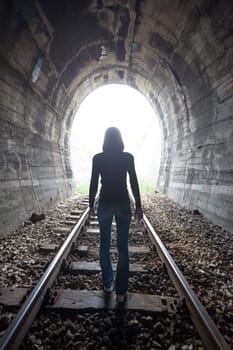 Man silhouetted in a tunnel standing in the center of the railway tracks looking towards the light at the end of the tunnel in a conceptual image